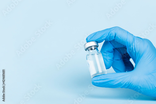 Hand in protective glove holds vaccine glass vial. photo
