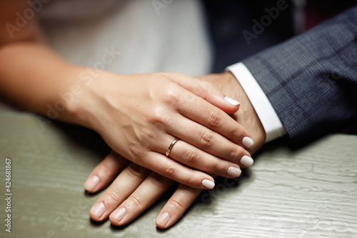 Woman's hand with a wedding ring on a man’s hand with a ring on a wooden table near a bouquet of flowers. Bride and groom, a young couple in a restaurant. Close-up of hands without face
