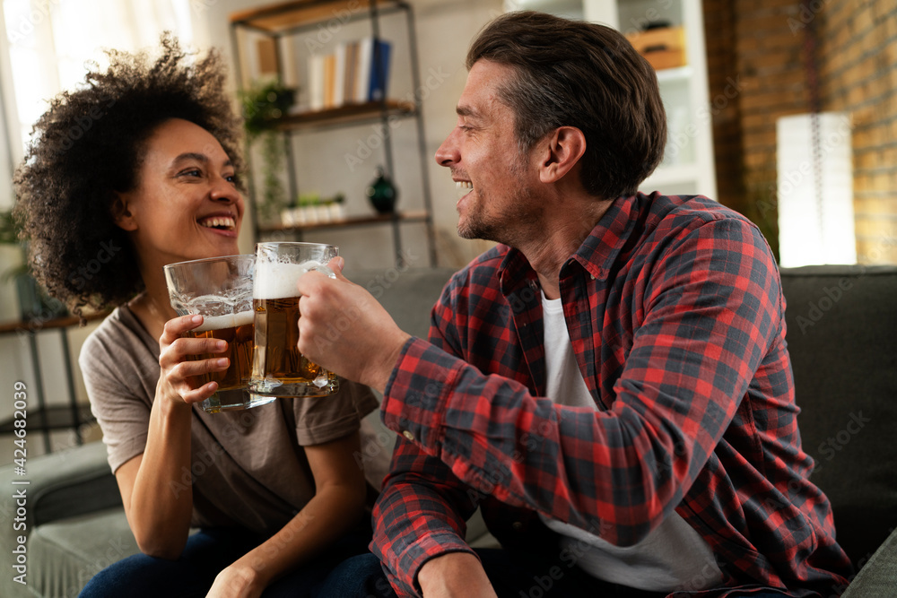Boyfriend and girlfriend drinking beer at home. Happy couple watching sports game on tv..