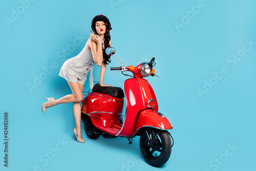 Full length body size view of charming slim girl making up visage maquillage posing near moped isolated on bright blue color background © deagreez