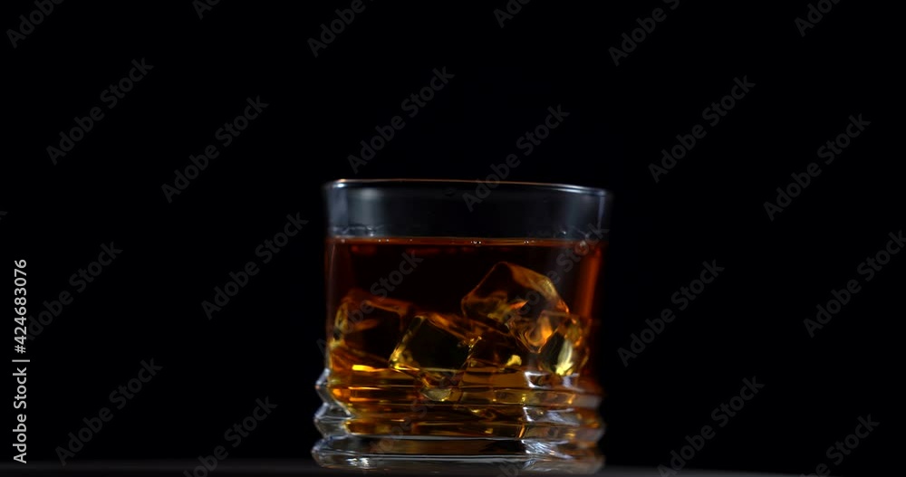 Golden whiskey in faceted glass with ice cubes rotating on black background macro. Alcoholic drinks, cocktail, alcohol. Pouring scotch into glass. Weekend afer hard work concept Golden whiskey in faceted glass with ice cubes rotating on black background macro. Alcoholic drinks, cocktail, alcohol. Pouring scotch into glass. Weekend afer hard work concept