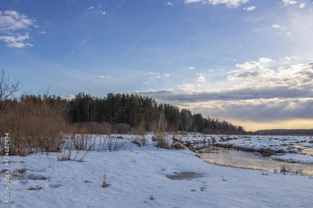 Sun through the clouds. Snow is melting. Early spring. Radiation of the river. Sun rays. Spring landscape