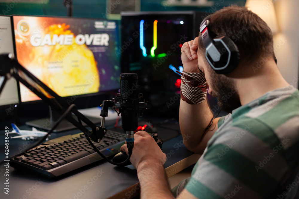 Videogame streamer losing videogame competition while wearing professional headset. Defeated gamer using modern controller for online tournament late at night in gaming room Videogame streamer losing videogame competition while wearing professional headset. Defeated gamer using modern controller for online tournament late at night in gaming room