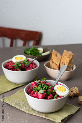 Russian salad vinaigrette in plates with boiled egg and black bread, salad of boiled and pickled vegetables and canned green peas