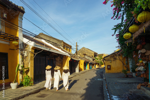 Street view of Hoi An ancient town in central Vietnam, with young girls wearing Vietnamese traditional dress Ao Dai walking on street