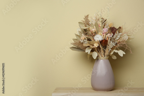 Beautiful dried flower bouquet in ceramic vase on wooden table near beige wall. Space for text