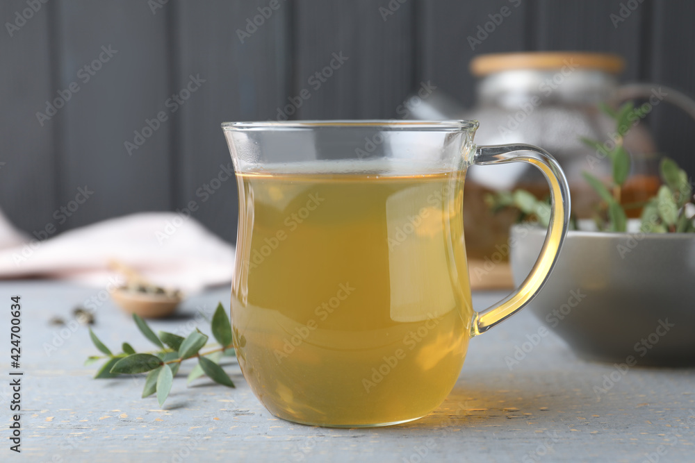 Glass cup of aromatic eucalyptus tea on grey wooden table, closeup Glass cup of aromatic eucalyptus tea on grey wooden table, closeup