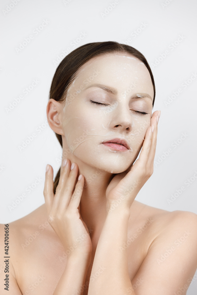 © photoaliona - Face Skin Care moisturizing Korean cosmetics concept. Portrait Of Beautiful woman applying and smoothing White Sheet Mask