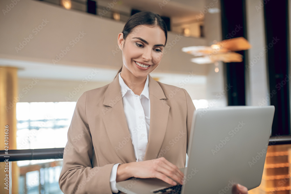 Young businesswoman in beige jacket standing with a laptop Young businesswoman in beige jacket standing with a laptop