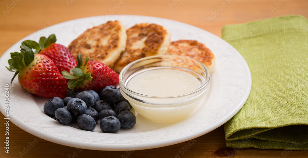 A plate with delicious cheese cakes, strawberries, blueberries and sweet sauce on a wooden background. Wide view.