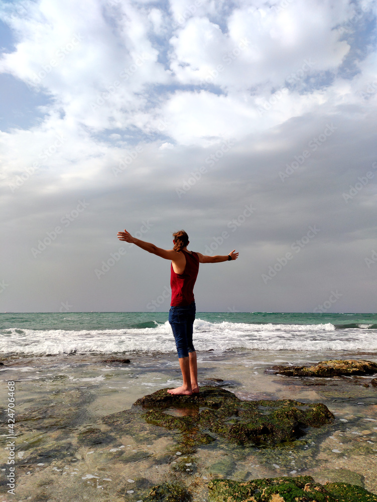 Young man on the beach seen from the back, with arms open enjoying the sensation of freedom in front of the sea.