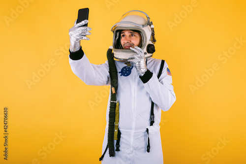 Εκτύπωση καμβά Male cosmonaut in space suit and helmet, taking a selfie with mobile phone, on yellow background