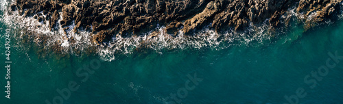 The ocean's wave hitting rocks. Blue water background. Aerial view. The natural landscape. Wallpaper. Ocean concept.