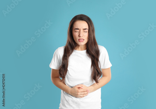 Canvastavla Young woman suffering from stomach ache on light blue background