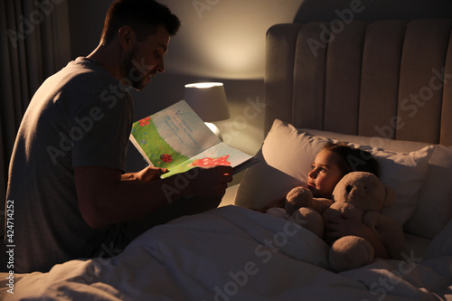 Father reading bedtime story to his daughter at home