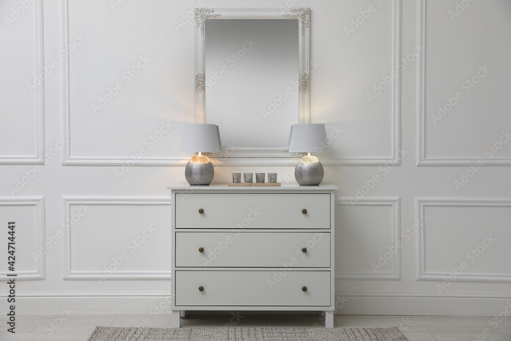 White chest of drawers with lamps near mirror in room. Interior design