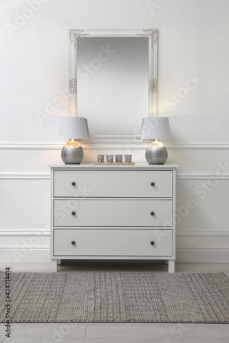 White chest of drawers with lamps near mirror in room. Interior design