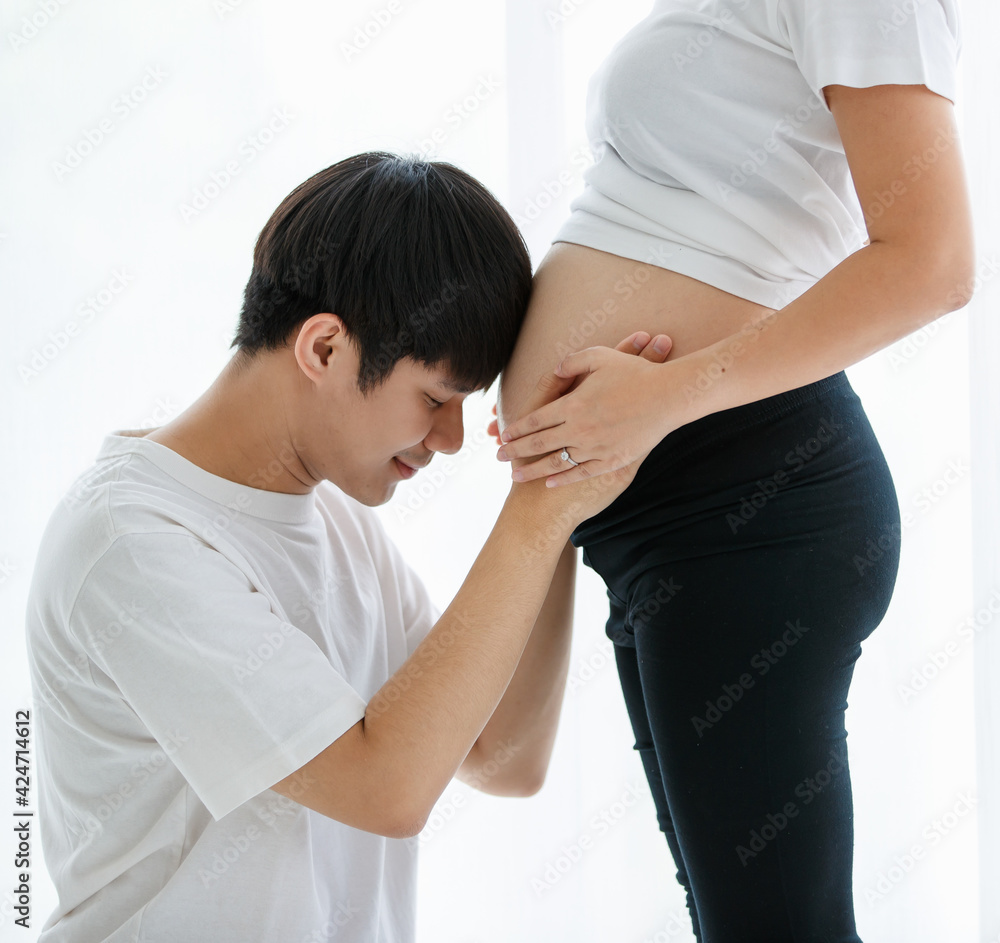 lovely family concept. Portrait of a young handsome Asian man and father wearing a white T-shirt sitting smiling happily while touching the belly of a pregnant woman lovely family concept. Portrait of a young handsome Asian man and father wearing a white T-shirt sitting smiling happily while touching the belly of a pregnant woman