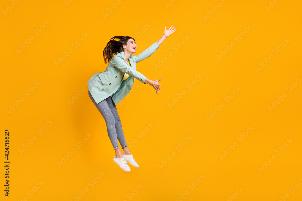 Full length photo of pretty cute young woman wear teal blazer jumping catching empty space isolated yellow color background
