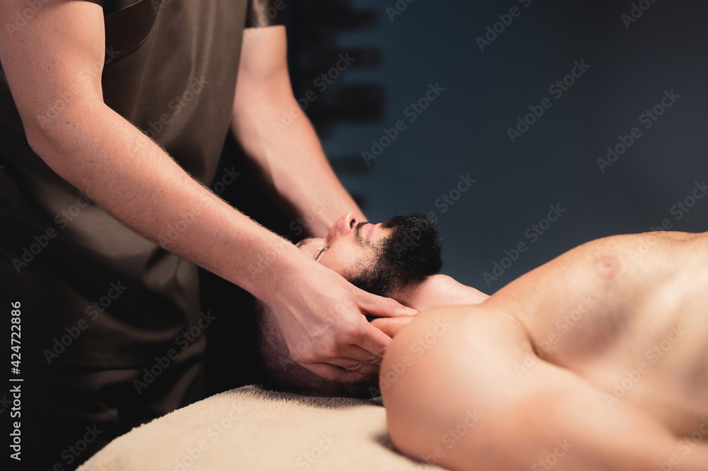 Professional neck massage to a bearded male athlete in a dark room of a spa massage room
