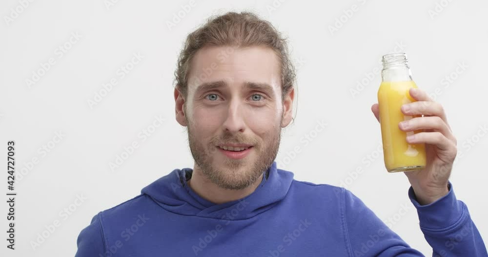 Attractive Smiling Guy Drinking orange Juice from Bottle Looking at the Camera. Having Positive Emotions, Healthy Smile, Teeth. Enjoying of drink. Standing at Studio. Wellness. Healthcare. Attractive Smiling Guy Drinking orange Juice from Bottle Looking at the Camera. Having Positive Emotions, Healthy Smile, Teeth. Enjoying of drink. Standing at Studio. Wellness. Healthcare.