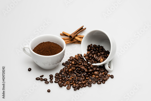 cinnamon sticks near cups with ground coffee and beans on white