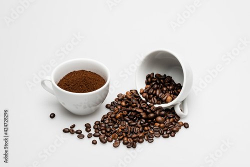Ground coffee and beans near cups on white