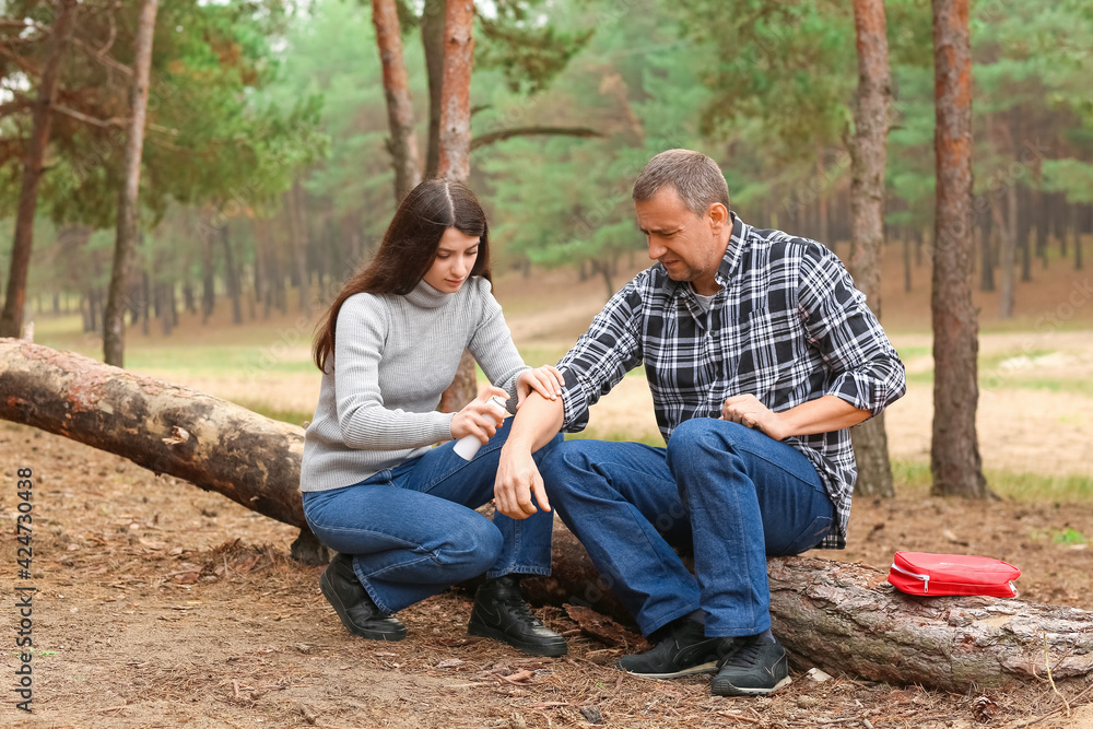 Young woman disinfecting injured arm of mature man in forest