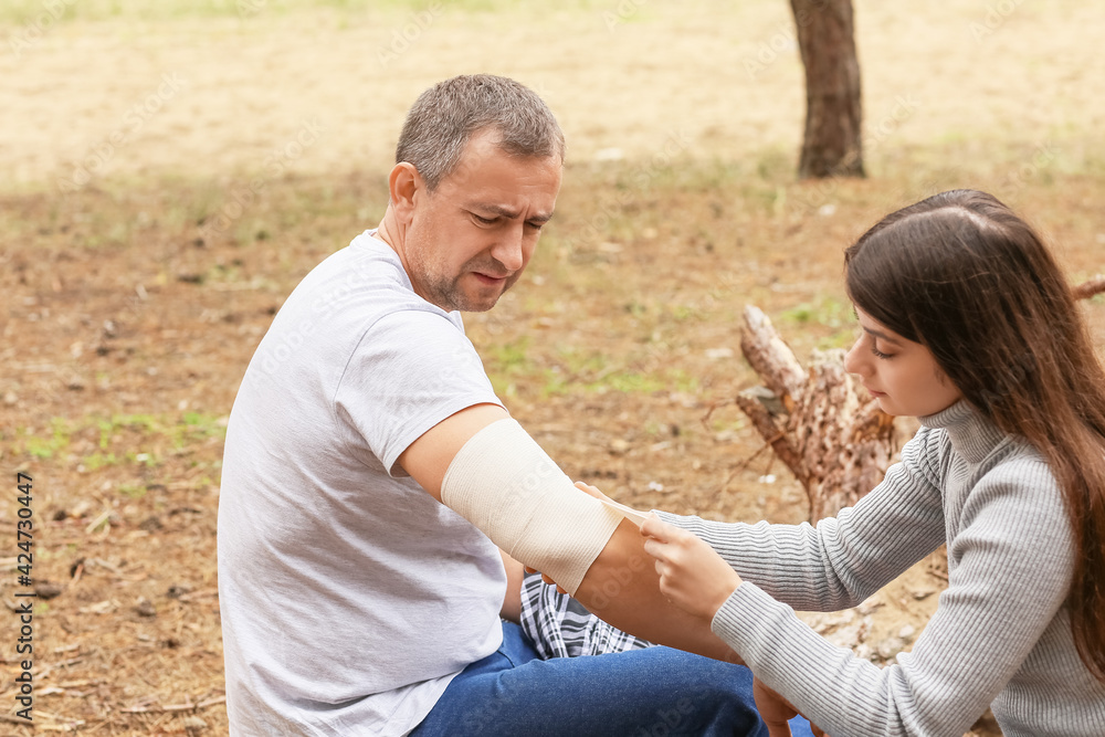 Young woman applying bandage on mature man's arm in forest