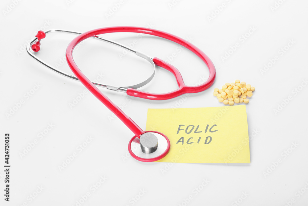 Stethoscope, text FOLIC ACID and pills on white background Stethoscope, text FOLIC ACID and pills on white background
