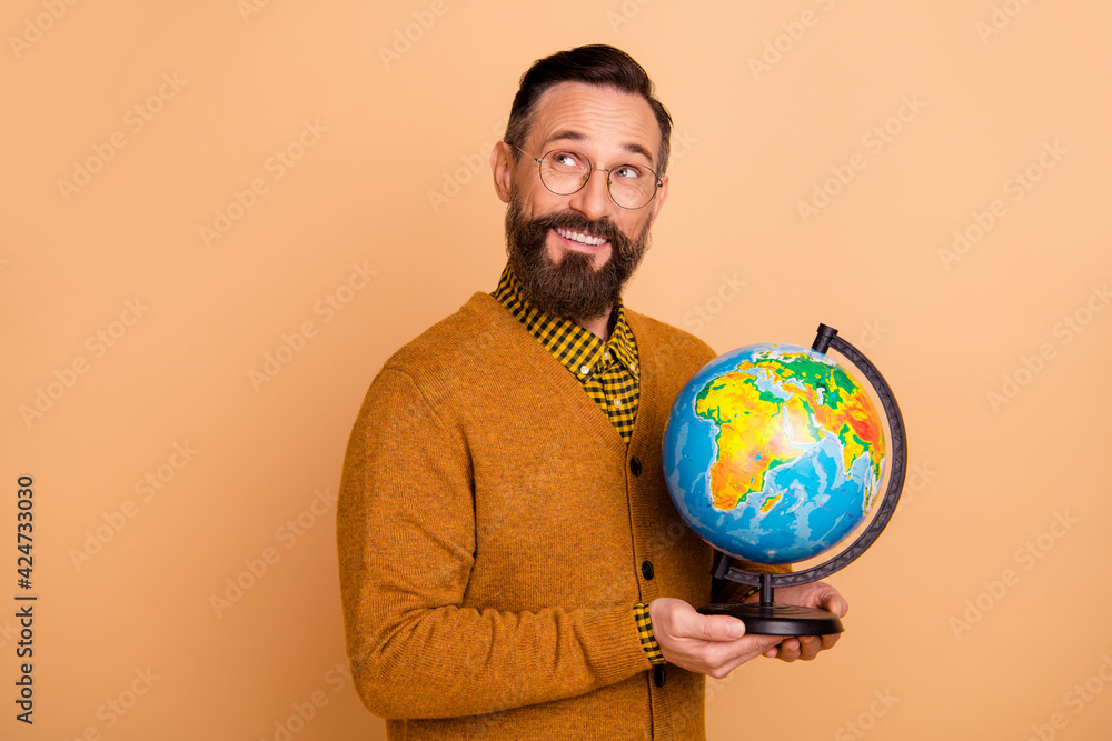 Photo of optimistic brown hair man hold globe look empty space wear spectacles brown sweater isolated on beige color background Photo of optimistic brown hair man hold globe look empty space wear spectacles brown sweater isolated on beige color background