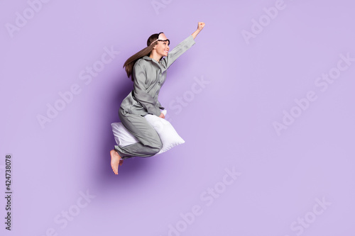 Full length body size photo of super woman riding on pillow flying high looking copyspace isolated pastel violet color background