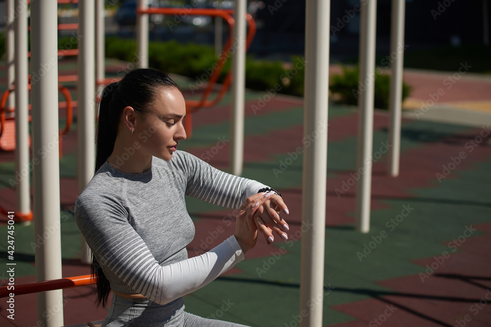 Obraz premium Young sportswoman checking her fitness tracker, pulse and heart rate, lost calories during outdoor workout, standing on a sports ground