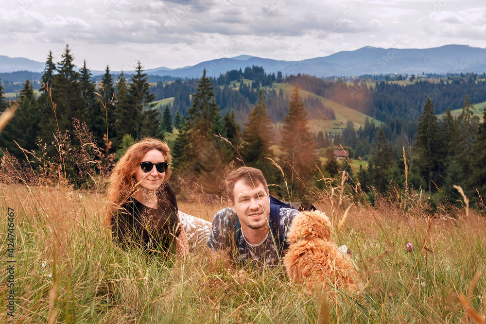 Man with a woman and a dog in the grass. Young couple with a puppy on a hike on a background of mountains