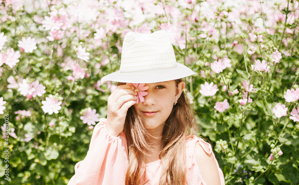 Fototapeta premium A girl in a beautiful pink dress and hat walks in a blooming garden.