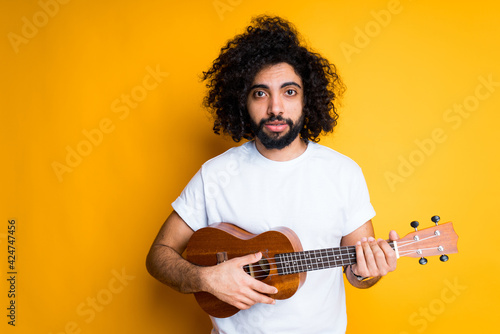 Sad african american guy with afro hairstyle and beard holds a ukulele in his hands and plays on it