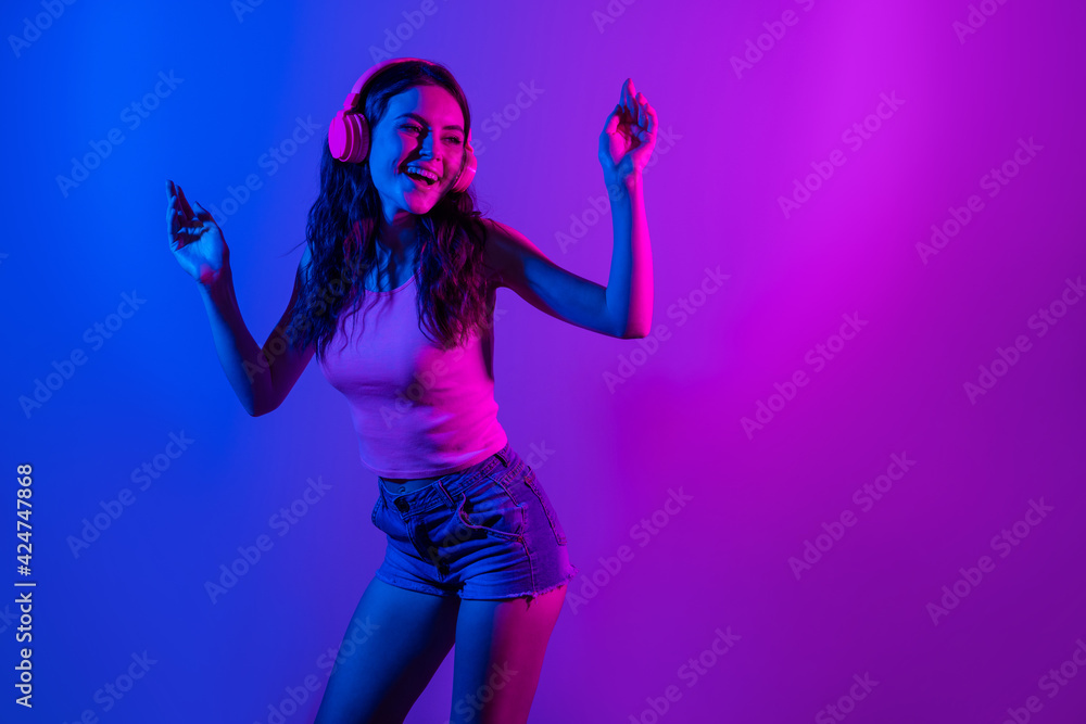 Photo of young smiling excited funky woman look copyspace dancing in headphones isolated on neon blue color background Photo of young smiling excited funky woman look copyspace dancing in headphones isolated on neon blue color background