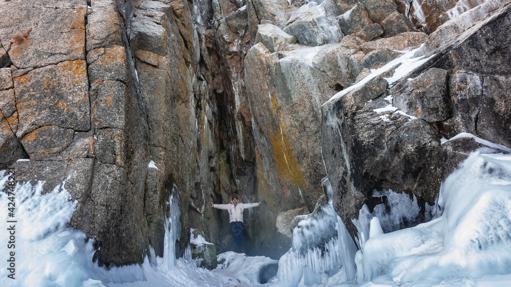 In a huge rock there is a crevice in which a man stands. His arms are spread apart, touching the walls of the cave. At the foot of the mountain - snow, ice splashes. Baikal.