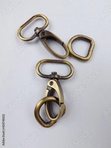 Haberdashery accessories, metal snap hooks or metal swivel clip snap hooks and D rings for bag strap, all in brass color. Isolated against white background. 