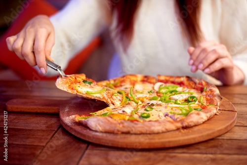 woman Hand takes a slice of sliced Pizza with Mozzarella cheese, tomatoes, pepper, olive. Italian pizza Margherita or Margarita on wooden table background