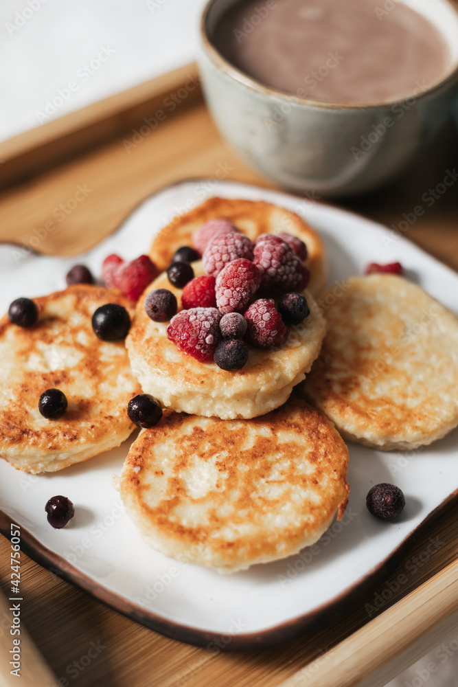 Cheesecakes with berries, a mug of cocoa on a tray against a white plaid background. Close up. Breakfast concept
Cheesecakes with berries, a mug of cocoa on a tray against a white plaid background. Close up. Breakfast concept