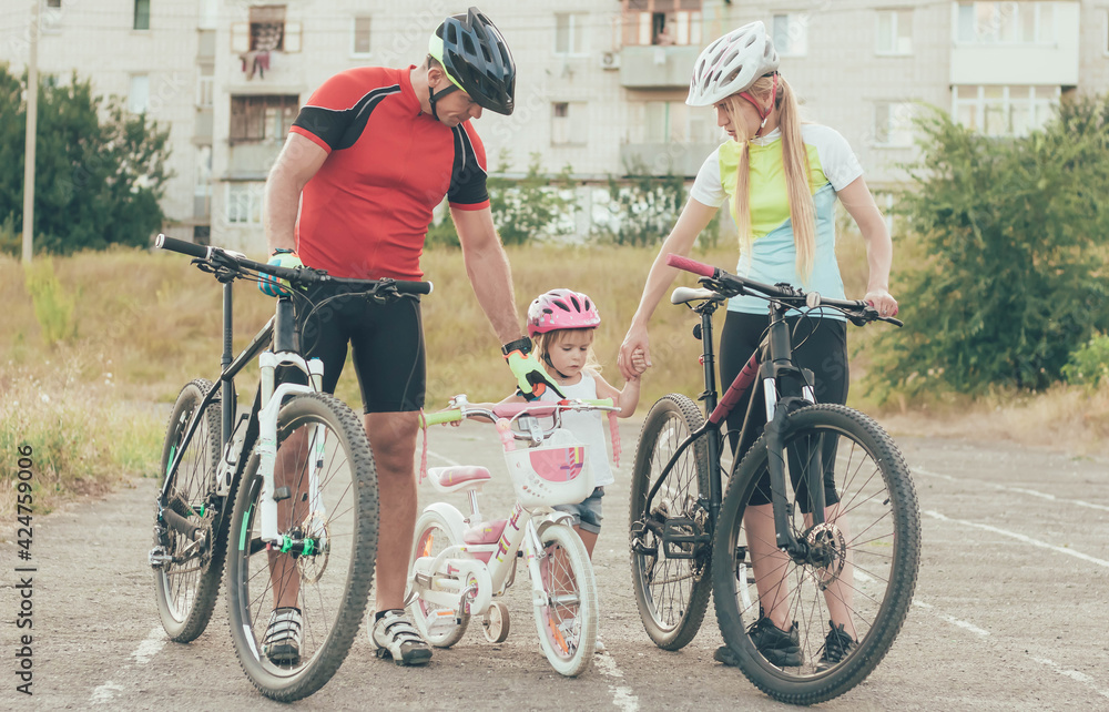 Fototapeta premium Mom and Dad are teaching little daughter to ride a bike in the stadium