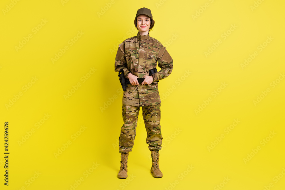 Full length portrait of charming satisfied girl standing hands hold tactical belt isolated on yellow color background Full length portrait of charming satisfied girl standing hands hold tactical belt isolated on yellow color background