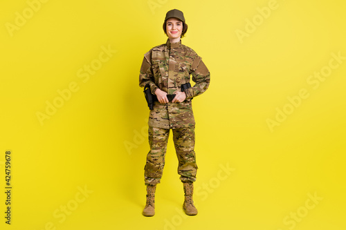 Full length portrait of charming satisfied girl standing hands hold tactical belt isolated on yellow color background