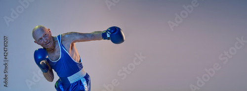 Senior man wearing sportwear boxing isolated on gradient studio background in neon light. Concept of sport, activity, movement, wellbeing. Copyspace, ad. © master1305