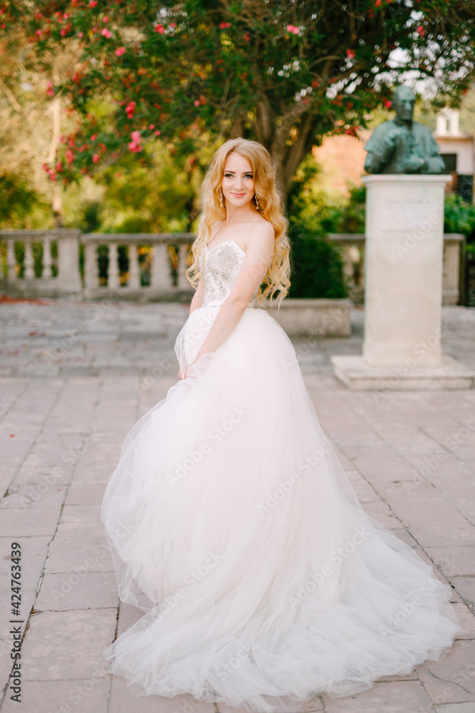 A blonde-haired bride in a lush white dress stands on the site near the ancient church in Prcanj 