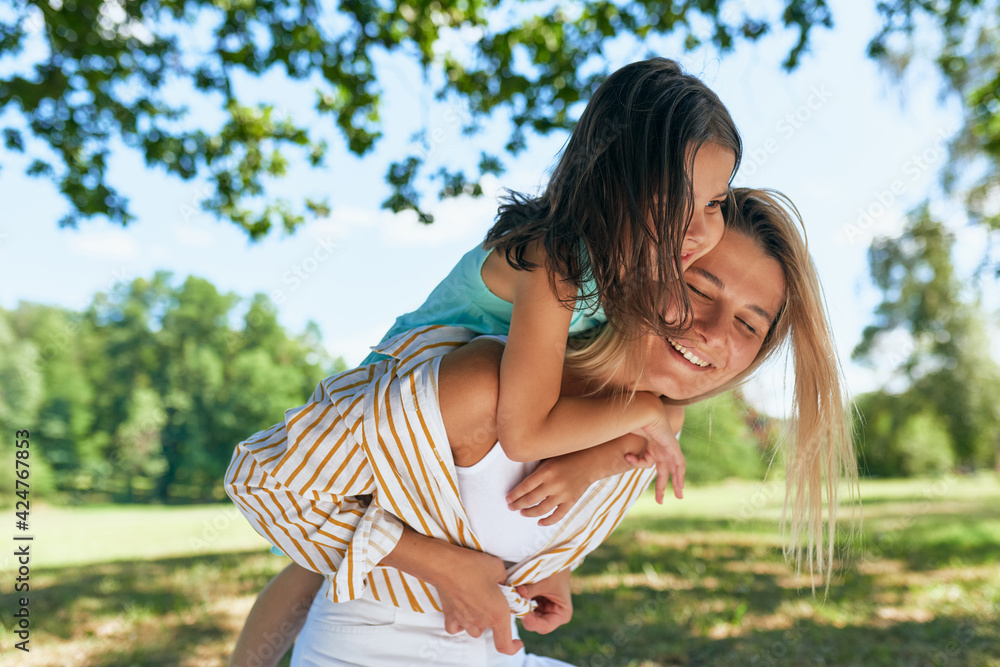 Naklejka premium Happy mother and her daughter playing in the park during the picnic. Happy woman and little girl smiling and spending time together on a sunny day. Mother's day.