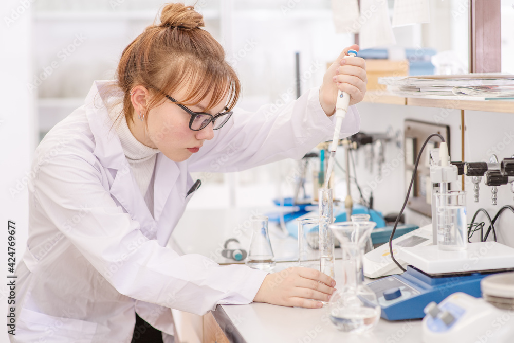 In a chemical laboratory, a girl laboratory assistant drips a solution into a measuring beaker with a special pipette In a chemical laboratory, a girl laboratory assistant drips a solution into a measuring beaker with a special pipette