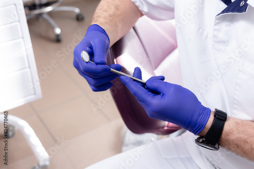 Dental mirror in male hands with blue medical gloves