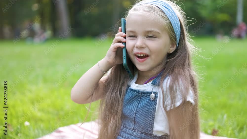 Happy little girl having conversation talking on mobile phone in summer park. Happy little girl having conversation talking on mobile phone in summer park.